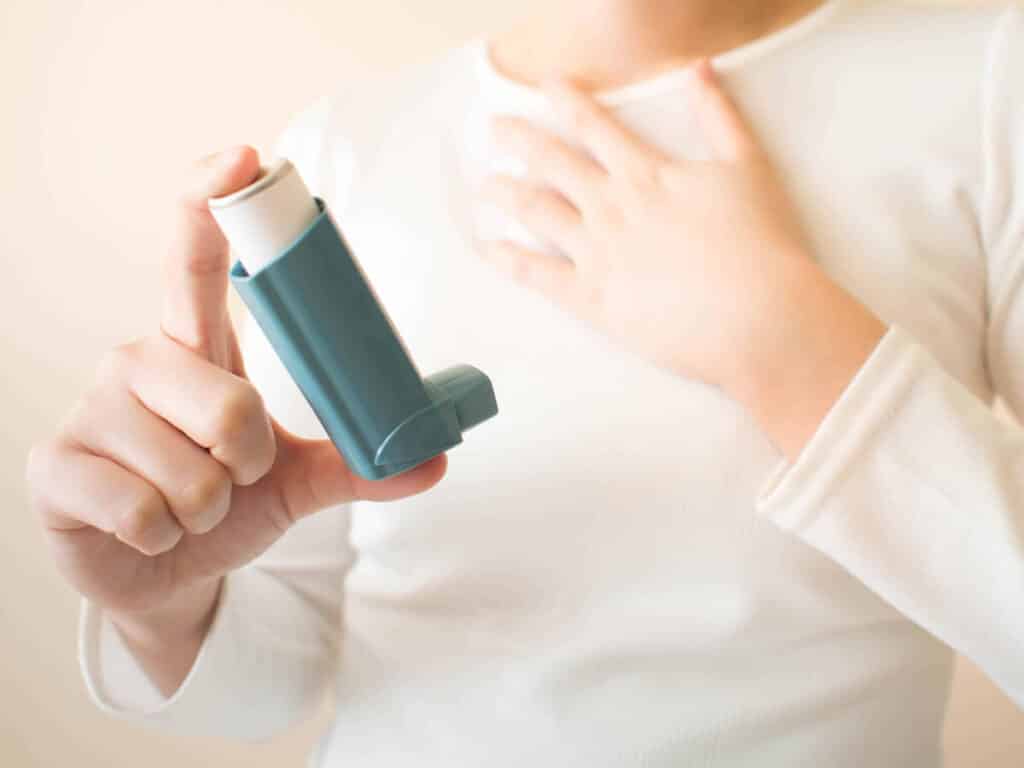 Young female in white t-shirt using blue asthma inhaler for reli