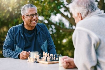 2 men smiling and enjoying a game of chess in the park.