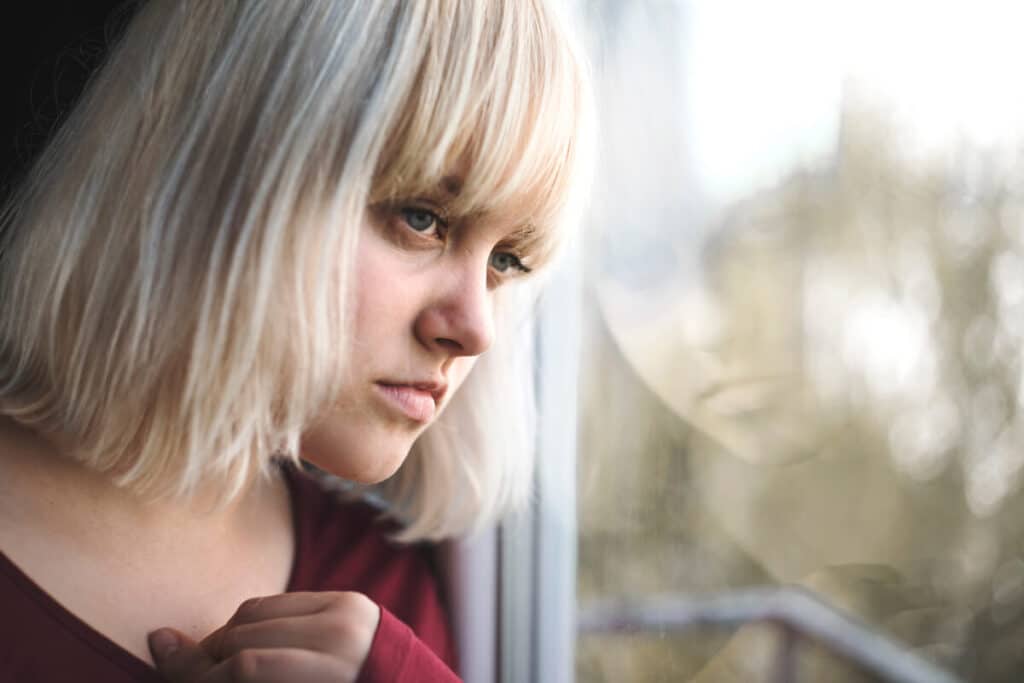 Close-up of a depressed young blond woman near a window at home.